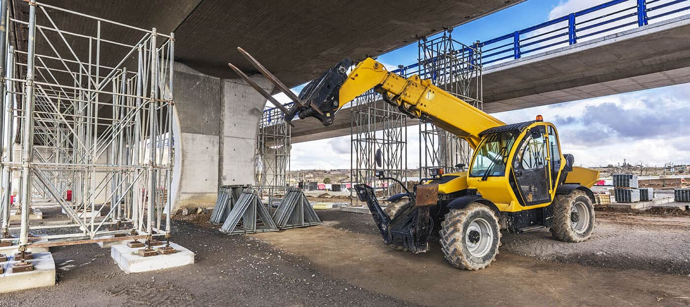 Telehandler with fork attachment driving on construction site